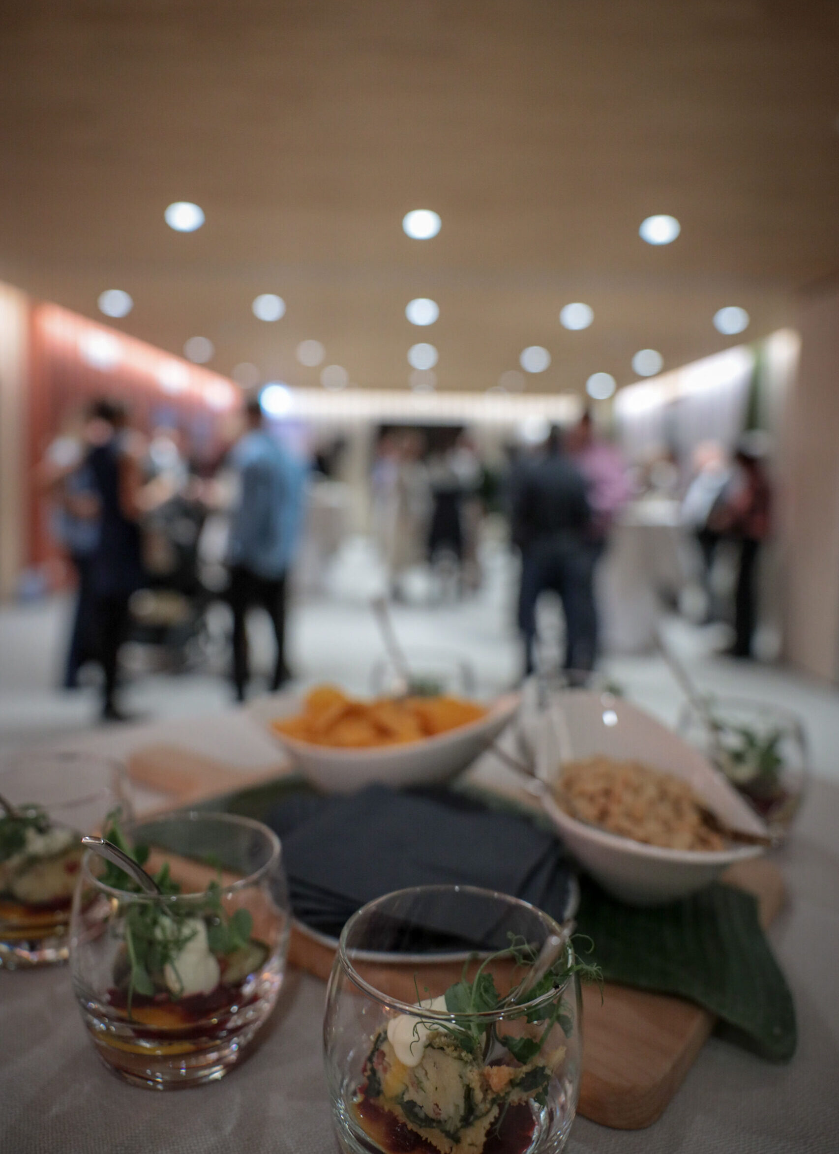 Apéro-Setting im AVES Hotel Savognin mit Gläsern und Häppchen im Vordergrund, Gäste im Hintergrund.