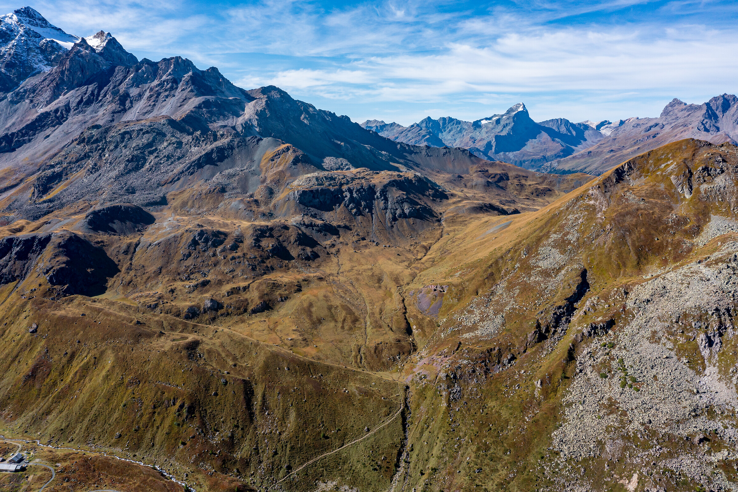 Hochgebirgspanorama mit braunen Alpwiesen, Felsformationen und schneebedeckten Gipfeln im Val Surses, Graubünden.