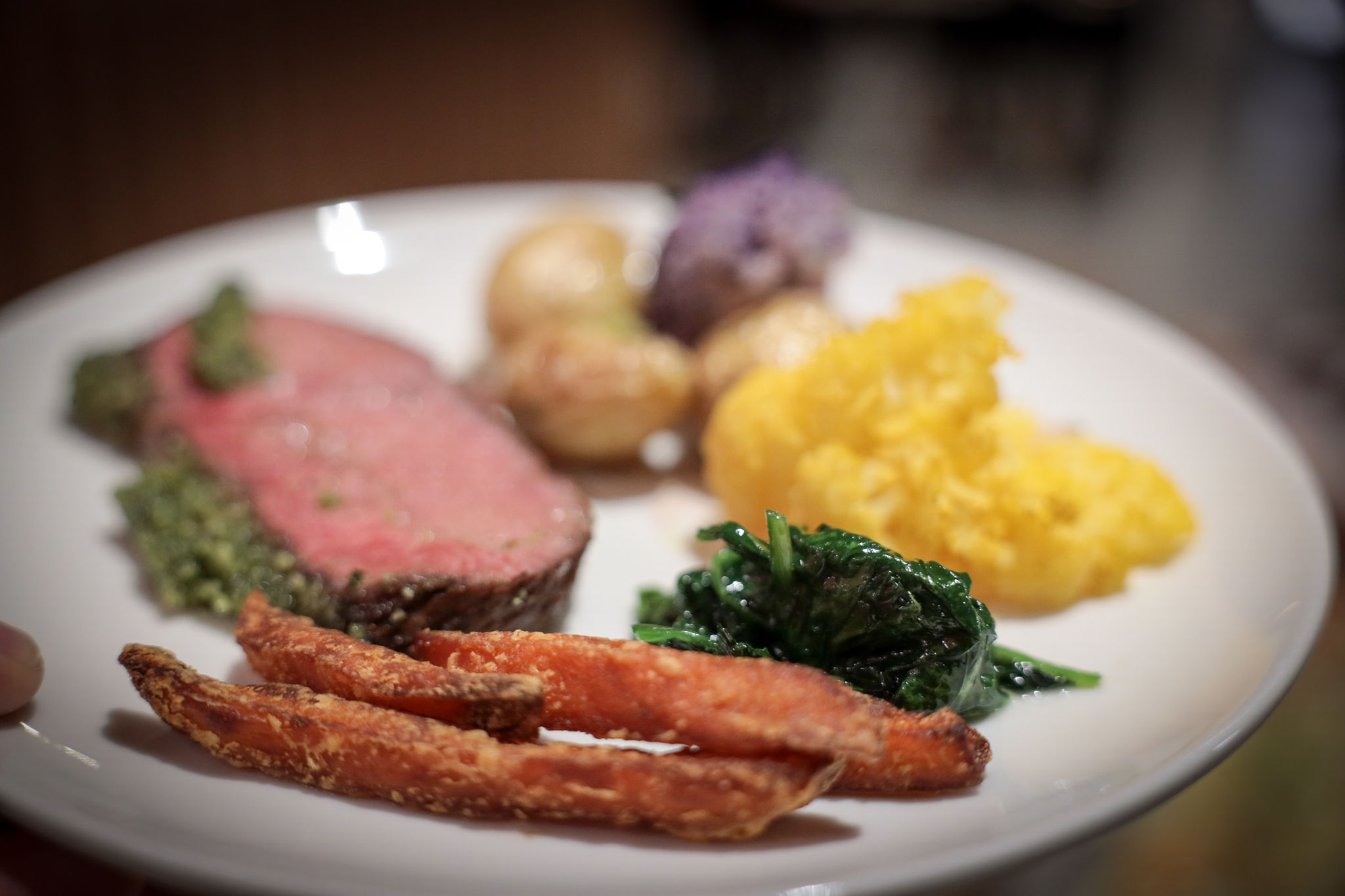 Rosa gebratenes Fleisch mit Kräuterkruste, serviert mit süssen Kartoffelspalten, Blattspinat, Kartoffelpüree und bunten Röstkartoffeln