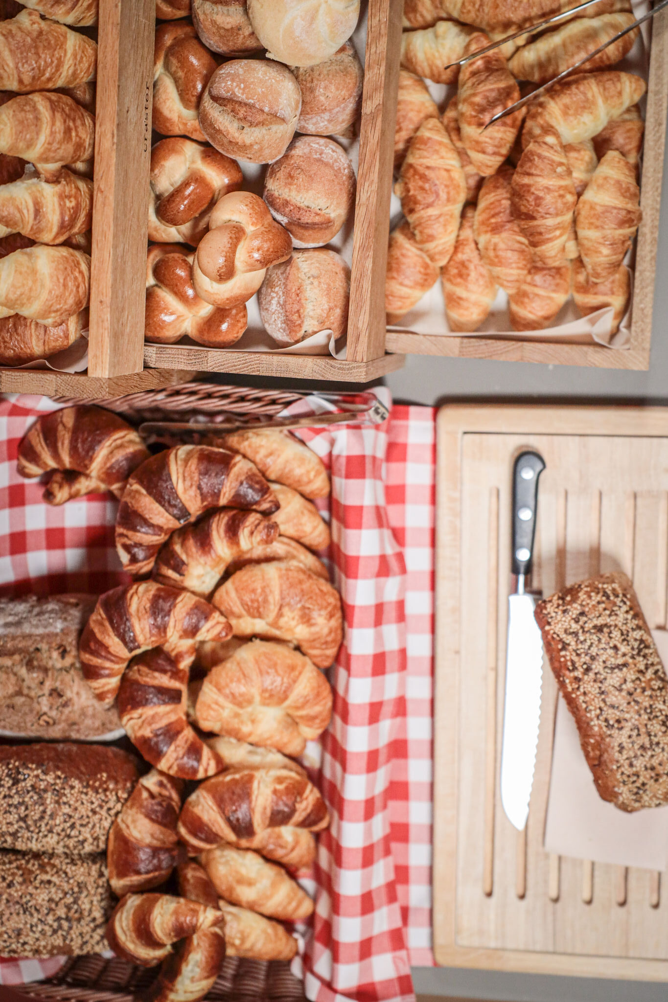 Nahaufnahme von frischen Croissants, Brötchen und Vollkornbrot in Holzkisten am Frühstücksbuffet